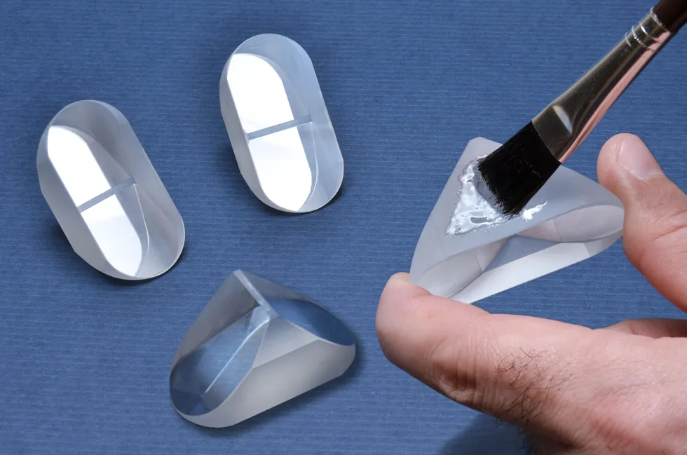 Hand brushing adhesive onto a clear optical prism beside three similar glass pieces